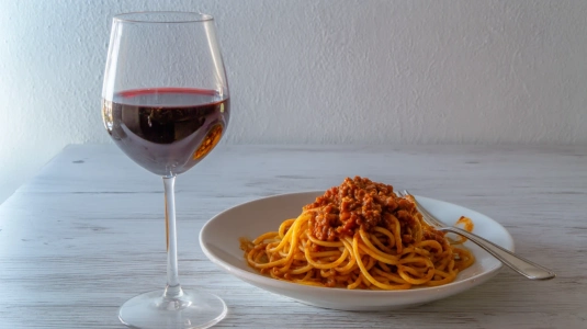 Glas rött vin bredvid en tallrik pasta med köttfärssås