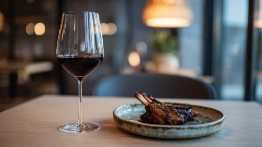 Glas med mörkt rödvin bredvid en tallrik med lammkött