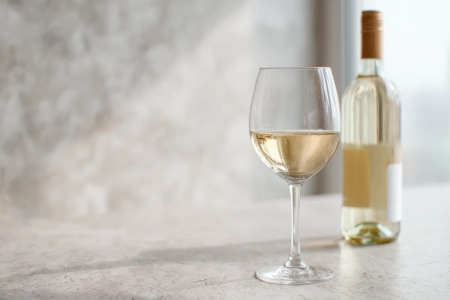 Glas med ljust chablis-vin bredvid en flaska på ett enkelt bord