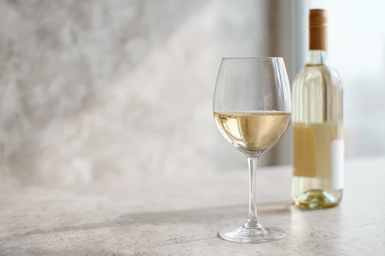 Glas med ljust chablis-vin bredvid en flaska på ett enkelt bord