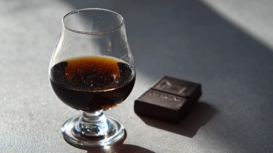 Litet cognacsglas med mörk, tjock öl bredvid en bit mörk choklad