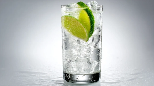 Gin och tonic i ett stort glas fyllt med is och en limeklyfta