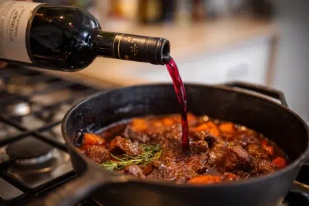 Rött vin som hälls i en puttrande köttgryta på spisen