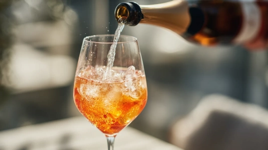 Prosecco hälls i en tunn stråle över Aperol och is i ett vinglas