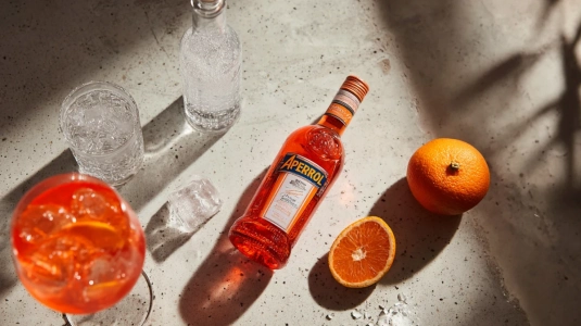Ingredienser till Aperol Spritz: Aperol-flaska, prosecco, sodavatten och en apelsin