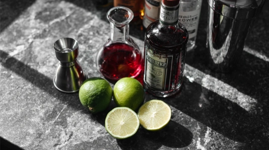 Vodka, Cointreau, tranbärsjuice, lime och cocktailshaker uppställda för en Cosmopolitan