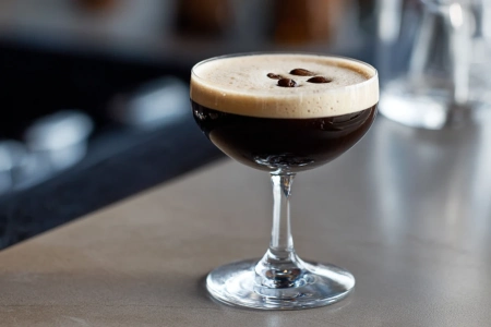 Espresso martini med tjockt skum och tre kaffebönor i ett coupeglas