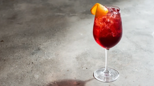 Djupt röd cava spritz med Aperol och Campari, garnerad med apelsintwist
