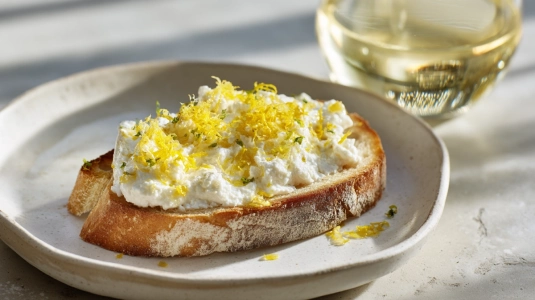 Rostad brödskiva med getost och citronzest bredvid ett glas Sauvignon Blanc