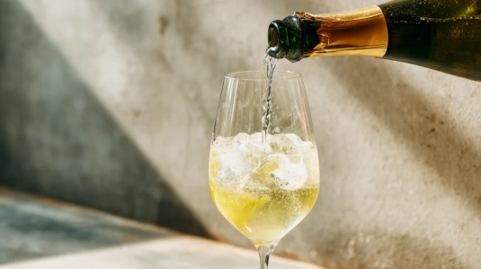 Prosecco hälls längs glasväggen i ett glas med limoncello och is