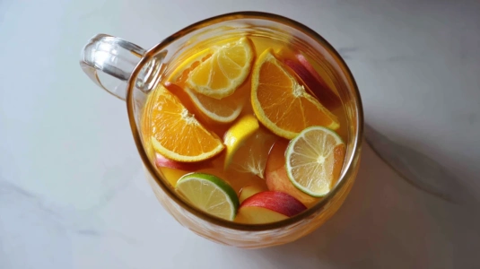 Skivad apelsin, citron och nektarin i en kanna med likör och apelsinjuice