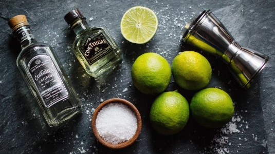 Tequila blanco, färska limefrukter och Cointreau uppställda med cocktailshaker och citruspress