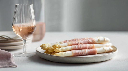 Vit sparris inlindad i skinka med ett glas rosé bredvid