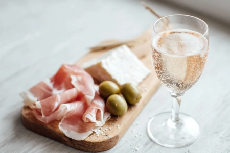 Bricka med charkuterier, getost och oliver bredvid ett glas prosecco