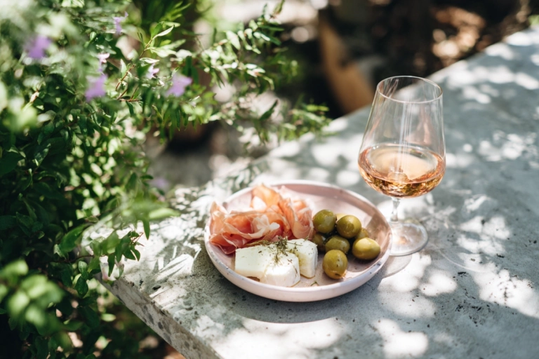 Tallrik med oliver, chèvre och prosciutto bredvid ett glas rosévin