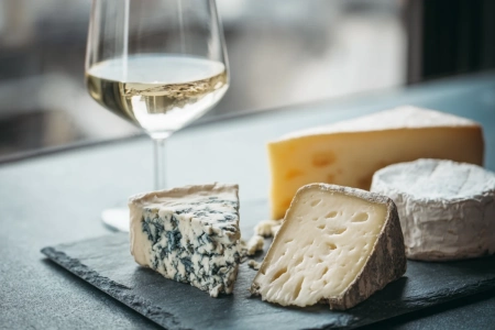 Ostbricka med olika ostar och ett glas vin bredvid